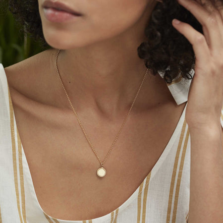 model's decollétage wearing a gold friendship disc charm on a gold belcher chain necklace